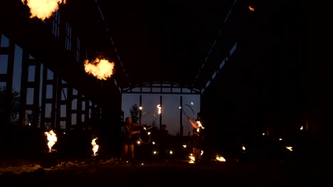 A-group-of-people-with-fire-and-torches-dancing-at-sunset-in-the-hangar-in-slow-motion.-Fire-show.